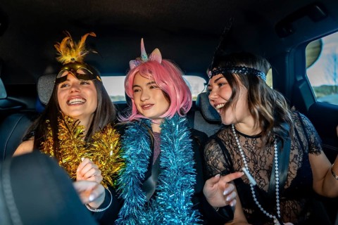 Young women friends celebrating new year's eve in costume, laughing and carefree in the back seat