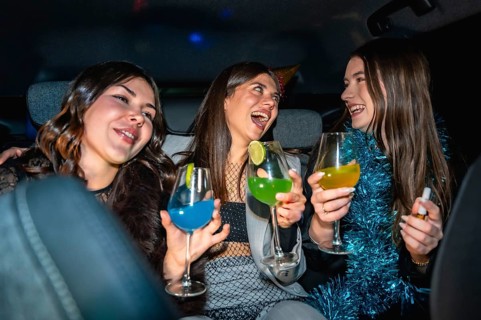 Three young women having fun traveling in a car at night, laughing and cheering with vibrant