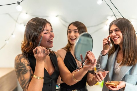 Three young women, best friends, getting ready and applying makeup at home before a new year's eve