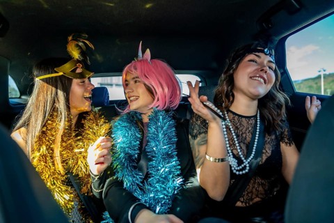 Three young women wearing festive costumes and tinsel garlands, smiling and laughing together while