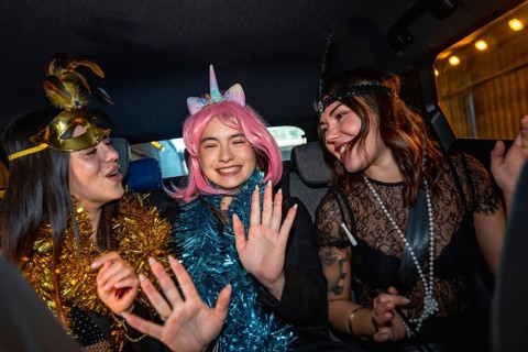 Three young women wearing festive costumes and garlands are happily laughing and dancing while