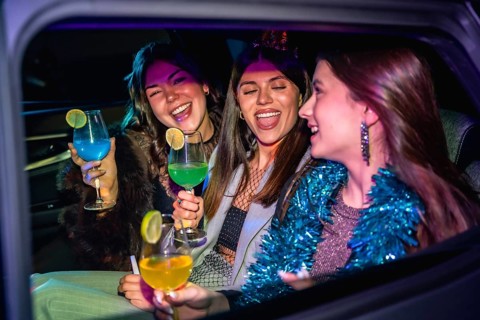 Three friends joyfully celebrating a festive occasion, laughing and holding colorful cocktails