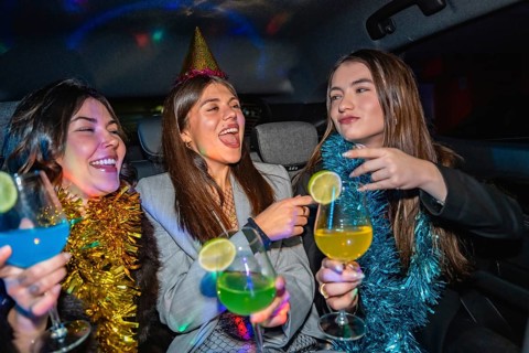 Three young women are happily celebrating a party in a car, enjoying colorful cocktails and good