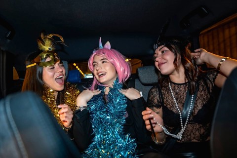 Three young women smiling, laughing, and having fun, dressed up in costumes with festive