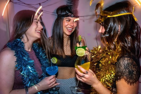 Young women friends laughing and cheering with colorful cocktails, celebrating together during a