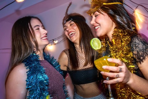 Three young women wearing party tinsel and costumes are happily celebrating new year's eve with