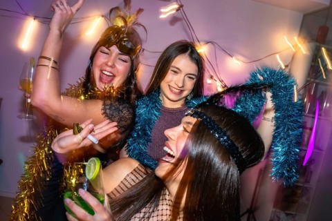 Three young women laughing and dancing, celebrating a festive new year's eve or costume party at