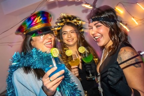 Three happy young women laughing and drinking colorful cocktails while celebrating a new year's eve