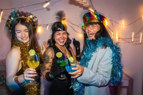 Three young women friends enjoying a fun new year's eve party, celebrating with colorful cocktails,