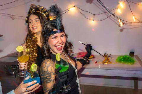Young women in 1920s style costumes celebrating at home with cocktails, string lights and disco