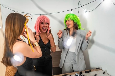 Three happy friends laughing and enjoying a costume party at home, wearing colorful wigs and