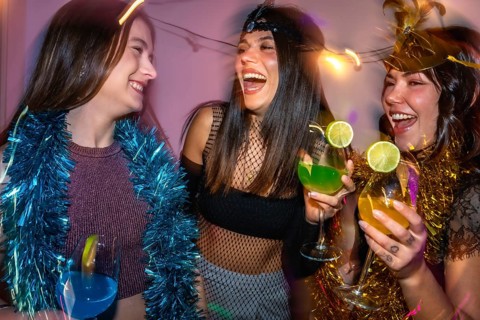 Group of women laughing and holding cocktails while celebrating with party decorations, enjoying a