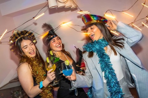 Three diverse young women happily celebrating and dancing together at a lively party, holding