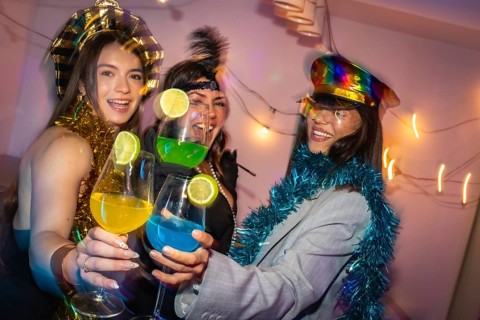 Three happy young women celebrating a party, toasting colorful cocktails with lime slices, laughing