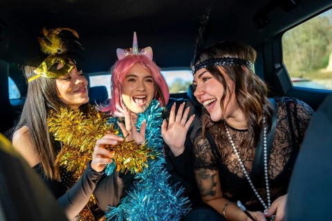 Happy young female friends wearing party costumes, tinsel garlands, and accessories, laughing and