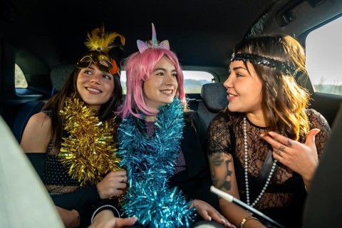 Three young women in colorful costume accessories and party attire laughing and talking in the back