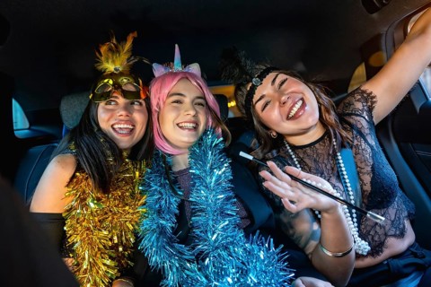 Three young women smiling and laughing, dressed in costumes with garland boas, celebrating a party
