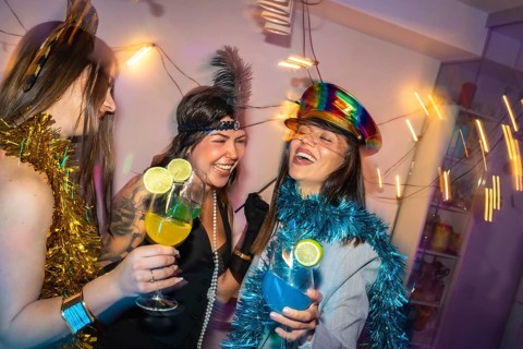 Young women friends enjoying a festive costume party at home, laughing and holding refreshing