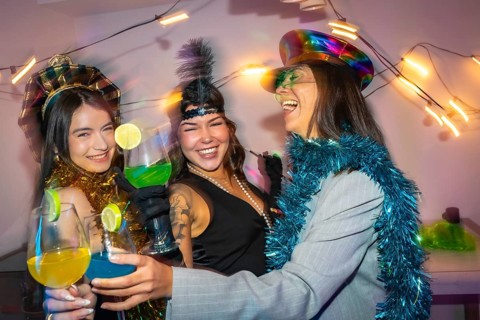 Three smiling young friends wearing party costumes and festive accessories celebrating a special