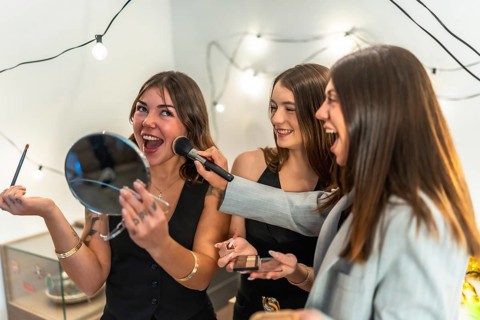 Three happy young women applying makeup and laughing together, smiling and enjoying their time