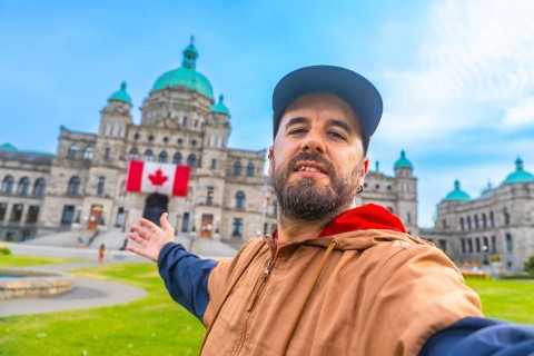 Happy bearded tourist taking a selfie with outstretched arms in front of the parliament buildings