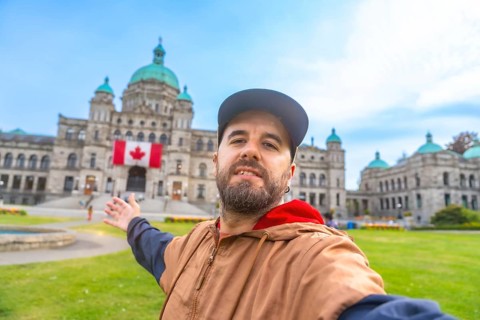 Happy bearded tourist taking a selfie with outstretched arm in front of the parliament buildings in