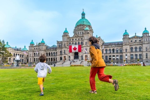 Mother and son running on the lawn in front of the british columbia parliament buildings in