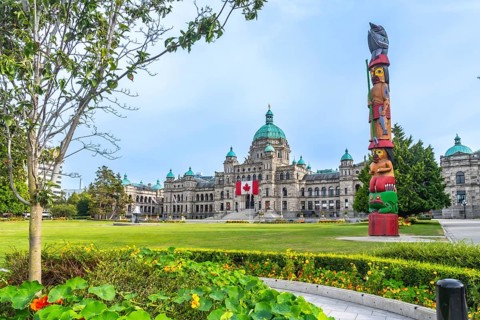 Canadian flag waving in the wind in front of the british columbia parliament buildings with a