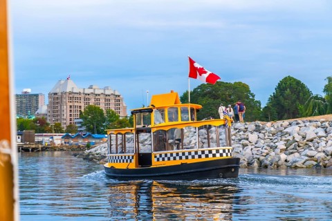 Yellow water taxi, flying canadian flag, leaving pier in victoria harbor with tourists walking on