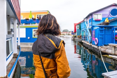 Tourist wearing a yellow jacket is enjoying the view of the colorful floating houses in fisherman's