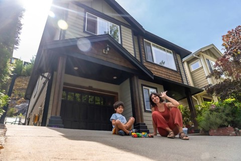 Mother and son are sitting on their driveway in front of their house, enjoying quality time