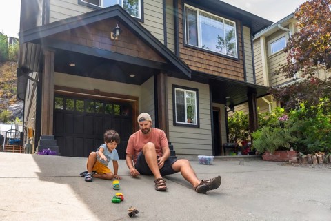 Father and son are sitting on their driveway, playing with a collection of toy cars in front of