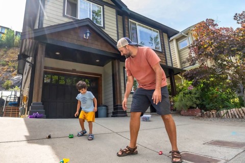Father and son are bending down and playing with toy cars on the driveway of their house in canada