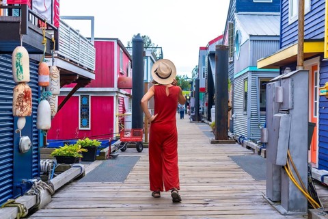 Tourist wearing a straw hat and a red jumpsuit is walking on a wooden boardwalk between colorful