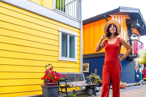 Tourist wearing a straw hat and red jumpsuit poses in front of the colorful floating houses of