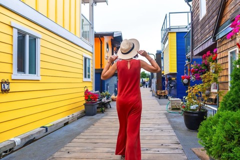 Tourist wearing a straw hat and red dress walking along the wooden boardwalk at fisherman's wharf
