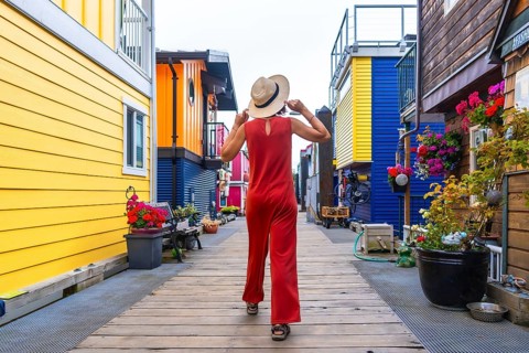 Tourist wearing a straw hat and red jumpsuit walking along a wooden walkway by vibrant floating