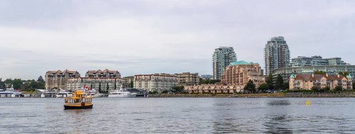 Yellow water taxi sailing in victoria, british columbia inner harbor with cityscape, condominiums,