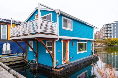 Colorful floating home with a white balcony and orange door reflecting in calm waters of victoria