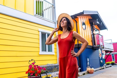 Happy female tourist wearing a straw hat and red dress is posing and smiling in front of the