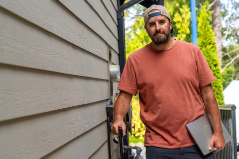 Maintenance worker walking alongside a residential building, carrying a laptop and various tools,