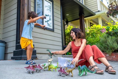 Happy mother and son enjoying quality time together, playing with dinosaur toys outside their house
