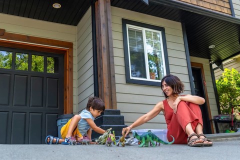 Mother and son sitting on the pavement in front of their house, joyfully playing with colorful