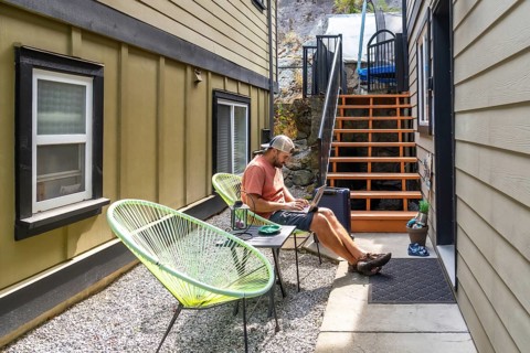 Young man working remotely on a laptop, lounging comfortably in a patio chair in his backyard,