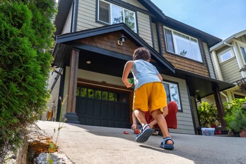 Two young brothers are happily playing with their toy cars on the driveway of their suburban home,