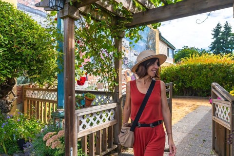 Smiling tourist in a straw hat and red jumpsuit walking out of a wooden gate in chemainus, a
