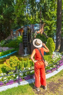 Female tourist wearing a straw hat and a jumpsuit is admiring a watermill and a colorful mural in a