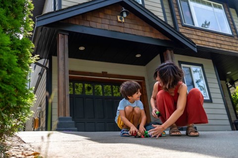 Mother and her young son are happily playing with toy cars on the driveway of their modern two