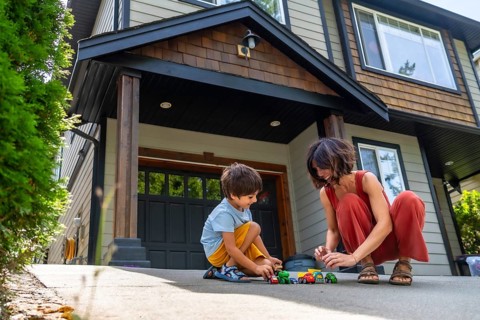 Mother and her young son are happily playing with toy cars on the driveway of their suburban home,