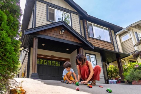 Mother and her young son are happily playing with toy cars on the driveway of their suburban home,